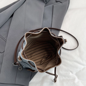 Denim blue bucket bag with drawstring closure and brown straps, top view showing interior