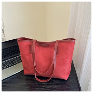 Large capacity red suede tote bag on desk featuring refined brand patch and slim straps