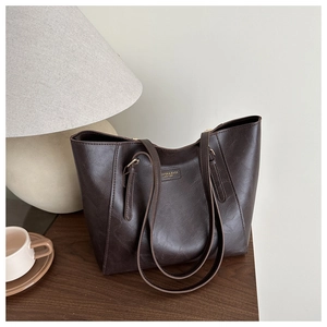 Detailed close-up of dark brown vintage PU leather tote with gold logo on wooden table