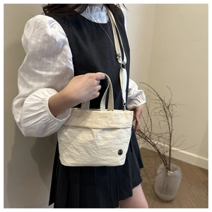 Detail of cream crossbody bucket bag with crinkle texture and wide fabric strap