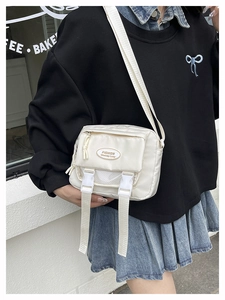Detail of off-white crossbody bag with buckle closure and adjustable strap on a model