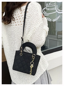 Detail of a black quilted crossbody bag with a vintage gold key charm and chain strap