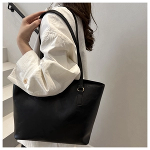 Detail of black leather tote bag with gold ring hardware shown on shoulder