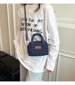 Detail of dark blue denim handbag with white contrast stitching and brown leather patch
