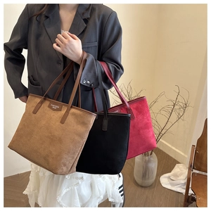 Suede tote bags in brown black and red displayed by a model in a minimal room