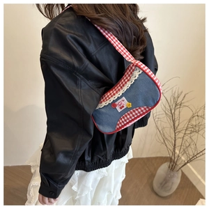 Détail du sac d'épaule en denim avec bordure à carreaux rouges et broderie cerise