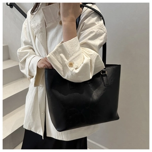 Detail of a large black leather tote bag with gold hardware shown on a female model