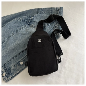 Detail of black nylon crossbody bag with metal M logo on denim jacket surface