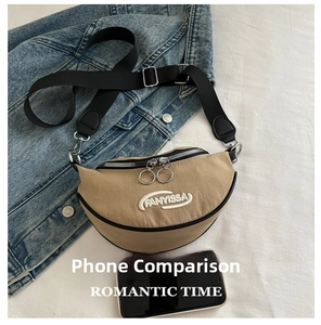 Detail of khaki crescent crossbody bag with white logo next to a smartphone