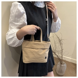 Detail of beige wrinkled nylon bag with silver metal logo and slim fabric shoulder strap