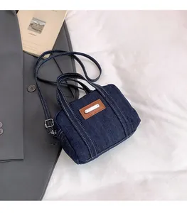 Detail of blue denim mini crossbody bag with brown leather label and double handles