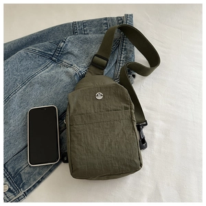 Macro shot of olive green nylon chest bag with metal M logo and adjustable strap