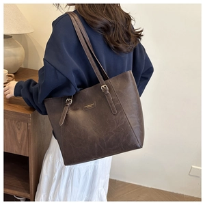 Dettaglio della borsa tote in pelle marrone scuro con logo in metallo e tracolla regolabile