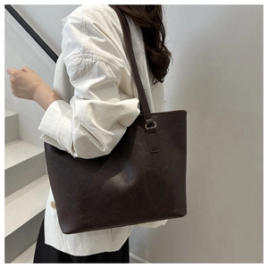 Detail of a large brown faux leather tote bag with gold buckles worn by a model
