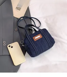 Detail of dark blue denim handbag with brown leather patch and white stitching contrast