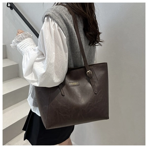 Detail view of large dark coffee tote bag with vintage metal logo and textured PU leather