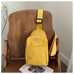 Detail of yellow nylon crossbody bag with metal M logo on a vintage wooden chair