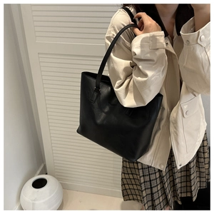 Close-up of black leather tote bag with lychee texture worn by a model in a minimal setting