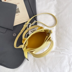 Litchi pattern yellow leather bucket bag with pearl pendant on grey suit background