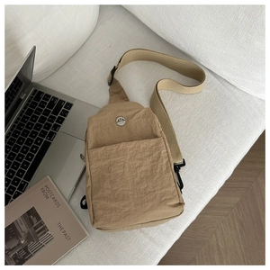 Dettaglio della borsa pettorale in nylon kaki con logo in metallo e tasca con cerniera