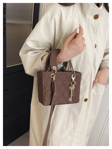Detail of a brown quilted handbag featuring fine stitching and gold key charm pendant
