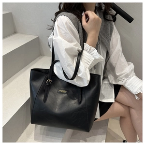 Detail of a black leather tote bag featuring a metal logo and adjustable shoulder strap