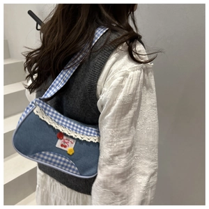 Close-up of blue denim underarm bag with red cherry embroidery and white lace details