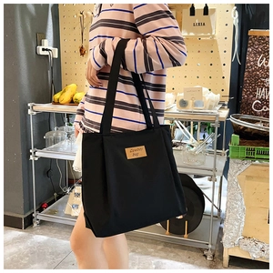 Detail of black canvas tote bag with brown leather label and thick woven shoulder strap