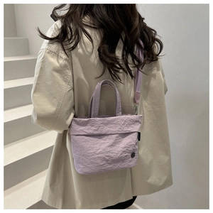 Detail of lavender pleated fabric texture and minimalist metal logo on a crossbody bag