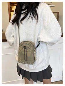 Détail du sac bandoulière en nylon vert olive avec cordon de serrage et broderie de marque