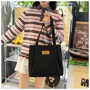 Detail of black canvas tote bag with brown leather label and adjustable shoulder strap