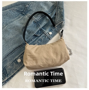 Detail of beige pleated fabric shoulder bag with silver chain and black leather handle