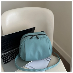 Close-up of a sage green nylon crossbody bag with dual zippers on a chair with a laptop