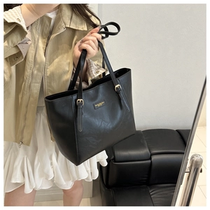 Detail of black textured tote bag with golden metal logo and adjustable buckle handle