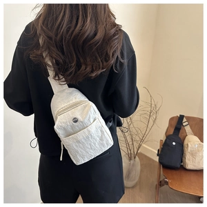 Detail showing white textured nylon chest bag with adjustable strap and front pocket