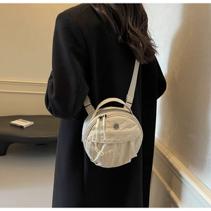 Detailed shot of a beige round nylon crossbody bag worn over a black wool coat