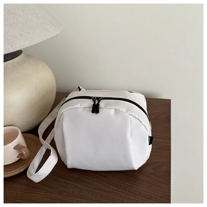 White round nylon crossbody bag with black zipper detail on a rustic wooden table