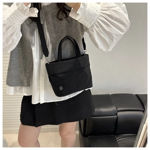 Detail view of a minimalist black canvas crossbody bag worn with a casual outfit