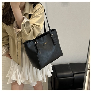 Detail of adjustable straps and gold metal buckles on a large black leather tote bag