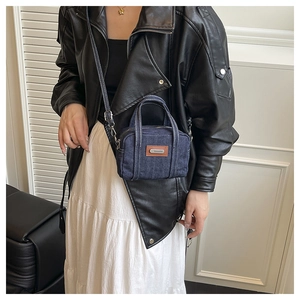 Close-up of a dark blue denim crossbody bag with white stitching worn by a model