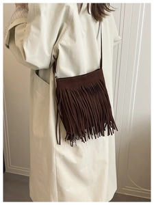 Detail of dark brown faux suede crossbody bag featuring long bohemian tassels and thin strap
