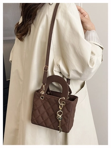 Detail of a brown quilted crossbody bag with golden key charm and sturdy top handle