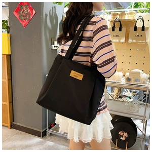 Close-up of a large black canvas tote bag with a brown leather logo label on model