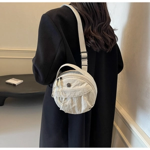 Detail of adjustable woven strap and metal logo on a beige nylon circular crossbody bag