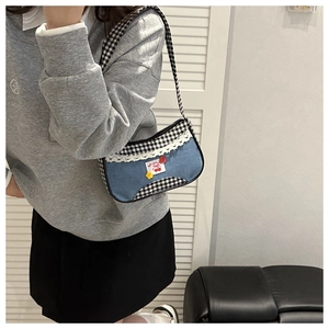 Detail of blue denim shoulder bag with lace trim, cherry patch and plaid straps