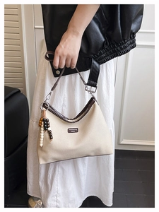 Détail du sac hobo en toile beige avec bordure en cuir et breloque en perles de bois