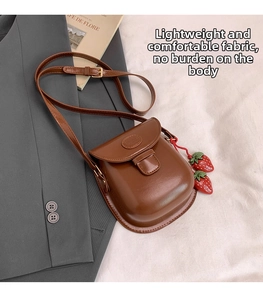 Close-up of brown PU leather mini saddle bag with decorative red strawberry charms
