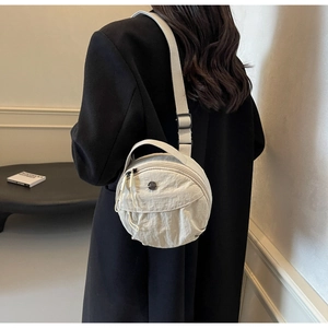 Model wearing a beige nylon round crossbody bag over a black winter coat in a minimalist setting