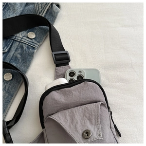 Detail of grey nylon crossbody chest bag showing zipper pocket and phone storage capacity