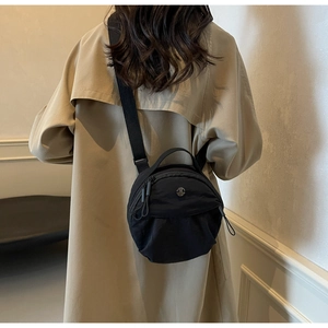 Detail of black nylon crossbody bag with metal logo and adjustable strap on a trench coat